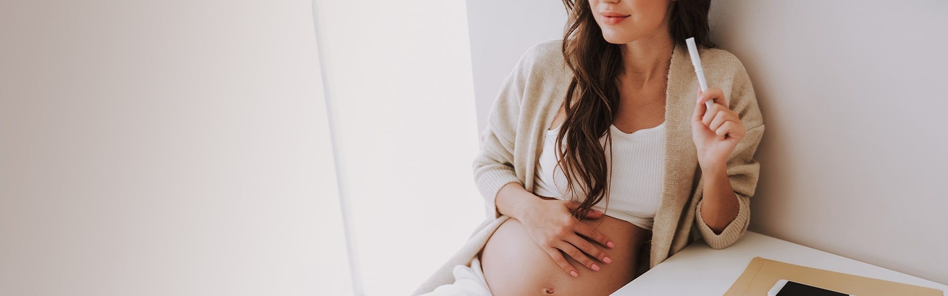 Attractive young woman holding hand on stomach and sitting in light room